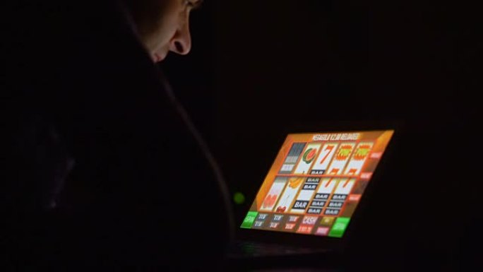 赌博成瘾男子在夜间笔记本电脑上的在线赌场老虎机前戴眼镜