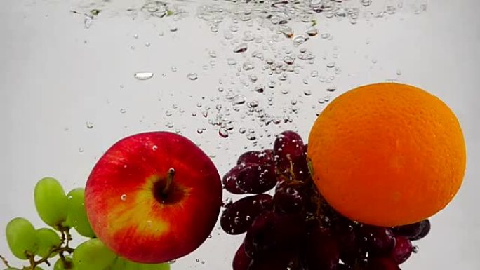 苹果，橙子和葡萄在慢动作中落入水中，并带有气泡。白色背景上的水果。