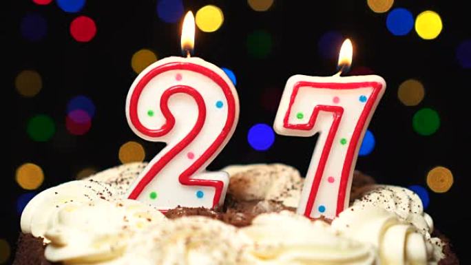 蛋糕上的27号-27岁生日蜡烛燃烧-最后吹灭。彩色模糊背景