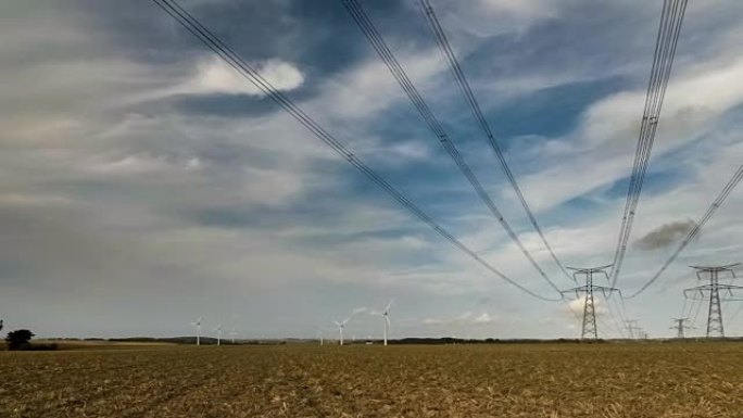 阴天，高压电力线，输电塔和风力涡轮机在野外的时间流逝。黄昏时的杆子和高架线剪影。电力工业与自然概念