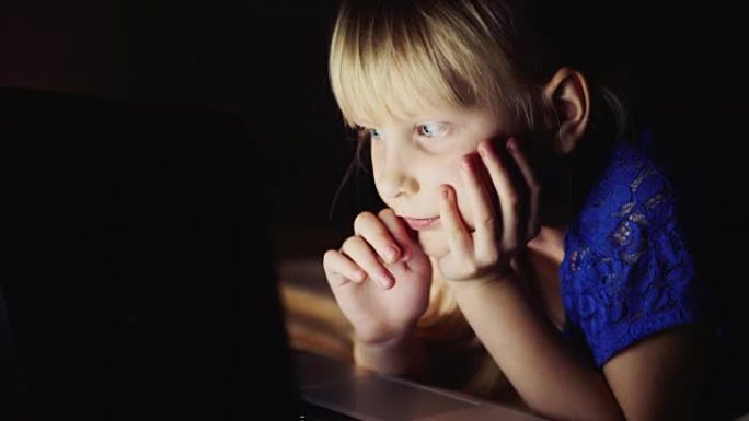 小女孩在笔记本电脑上看起来很卡通。夜光笔记本电脑屏幕照亮孩子的脸