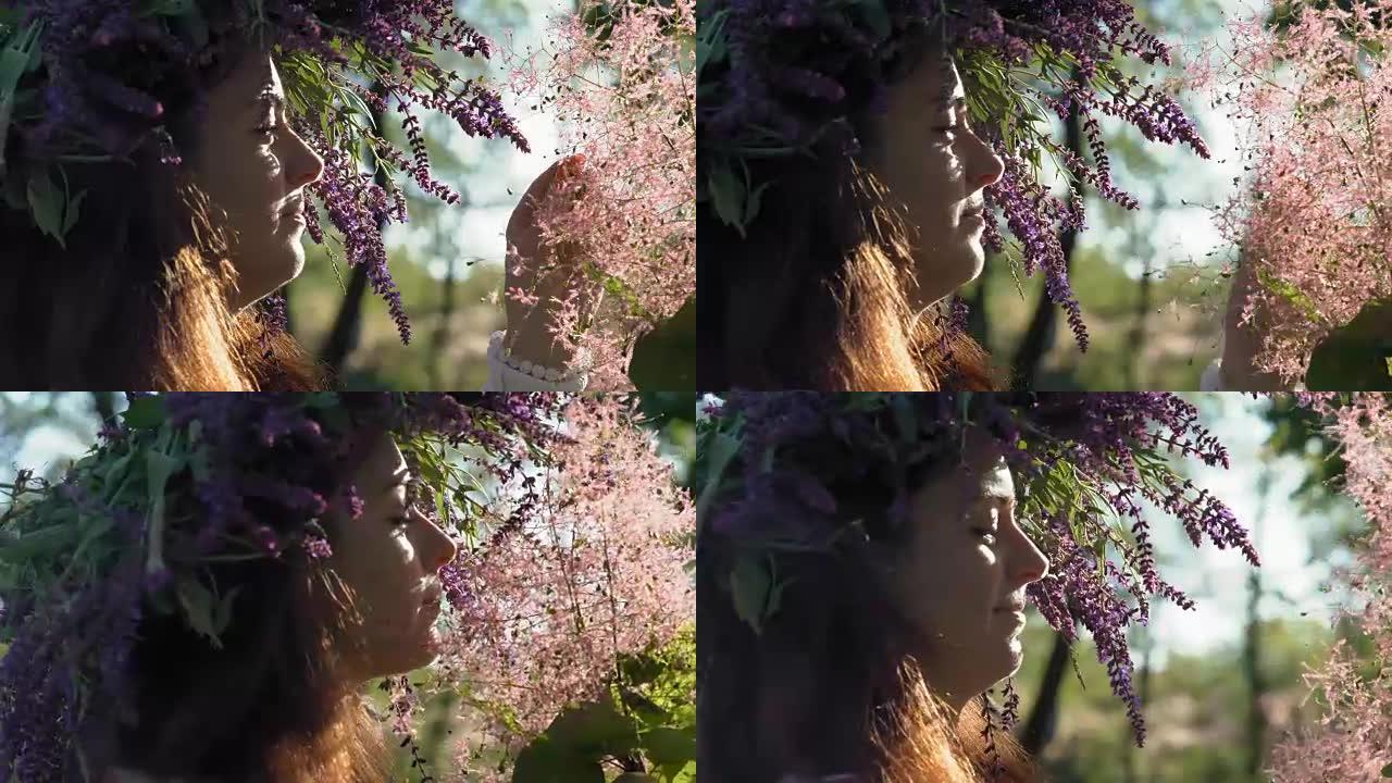 特写，头上有矢车菊花环的美女看起来在树林里盛开粉红色的灌木