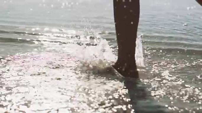 一个年轻女子的腿沿着海岸行走。女人沿着海岸奔跑，溅海水，慢动作。女人赤脚跑到浅层透明的海水里。