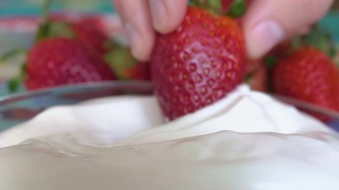 一只手将成熟的草莓浸入白色奶油中。美味的夏季收获。素食主义者。特写。