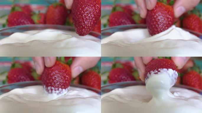 一只手将成熟的草莓浸入白色奶油中。美味的夏季收获。素食主义者。特写。
