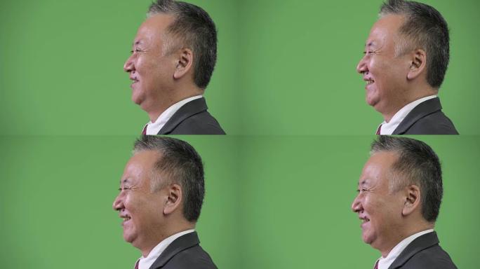成熟的日本商人在绿色背景下微笑的侧面视图