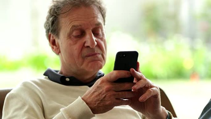 富有表现力的退休老人全神贯注于智能手机设备上的内容。坦率的真实生活中老人关注他的手机技术和4k电子邮