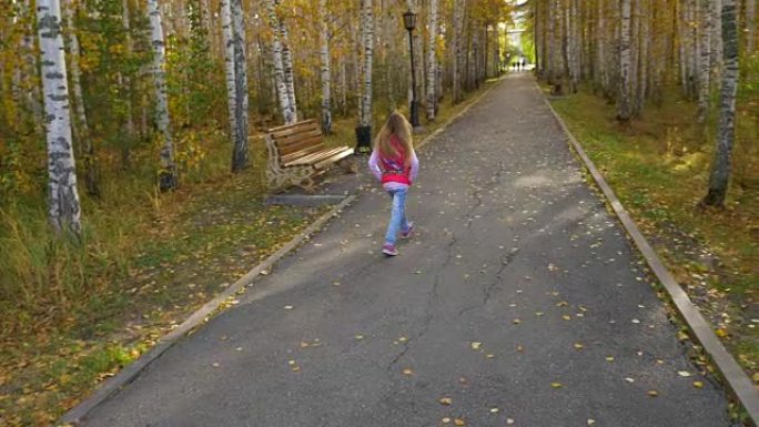 金发碧眼的长发女孩在秋季公园的小巷里奔跑。头发摆动的速度减慢。