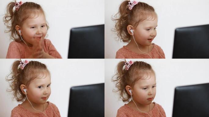一个戴着耳机的小可爱女孩微笑着看着屏幕监控电脑。有趣的孩子看电视、视频、卡通或玩游戏的应用程序