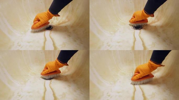 一个男人的手戴着橙色橡胶手套，用刷子清洁浴缸水槽。一般房屋清洁
