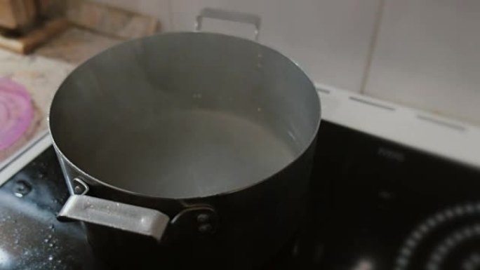 一个男人的手的特写打开了一锅开水的盖子。