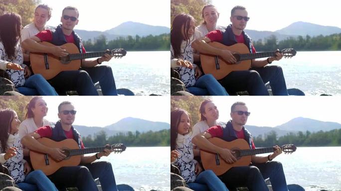 一群快乐的朋友在海边的夏天在山河旁边弹吉他唱歌。3840x2160