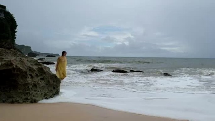 印尼巴厘岛大雨中海滩上穿着黄色雨衣的年轻女子