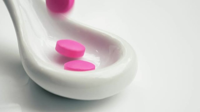 药品粉色药丸落入白色勺子。孤立在白色背景上。勺子上的粉色药丸细节。