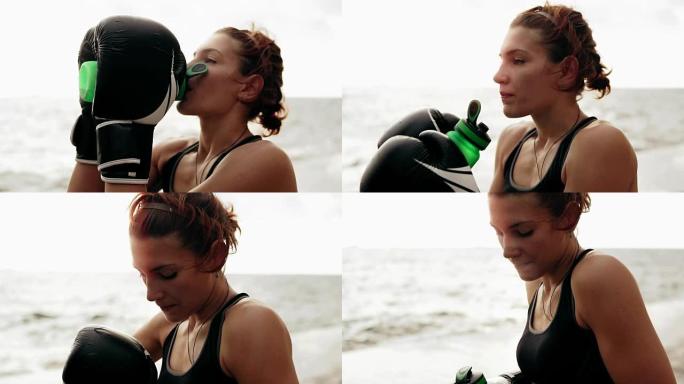 口渴的女拳击手戴着手套休息一下，训练后从水瓶里喝水。海边训练的美女