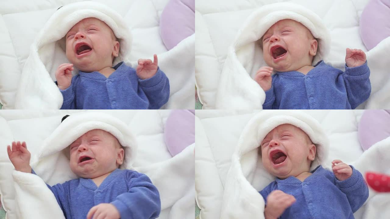 新生儿哭泣的男婴。新生儿在蓝色针织毯子下的床上又累又饿