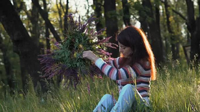 美丽的女孩采摘矢车菊花环，早上坐在森林的空地上