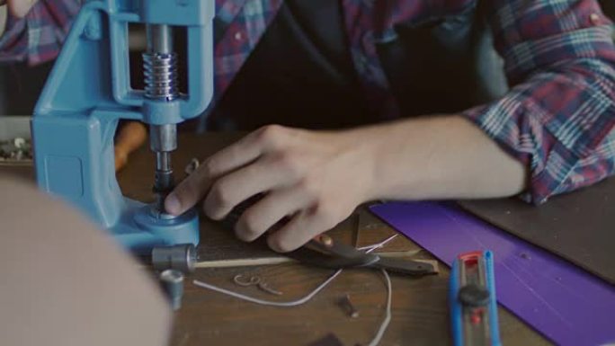 皮革制造商将金属按钮插入皮带。工匠工作