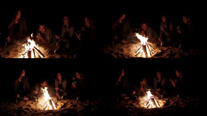 圆形摄像机运动: 多种族的年轻男孩和女孩在深夜坐在篝火旁唱歌和弹吉他。欢快的非洲裔美国人在炉火旁弹吉