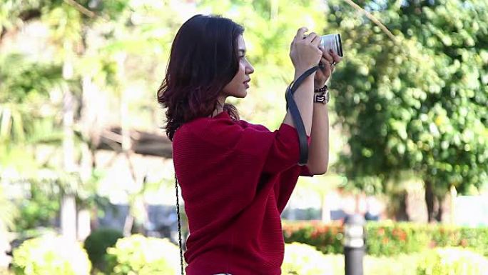 穿着红色连衣裙的年轻亚洲女孩在公园里拿着相机拍照