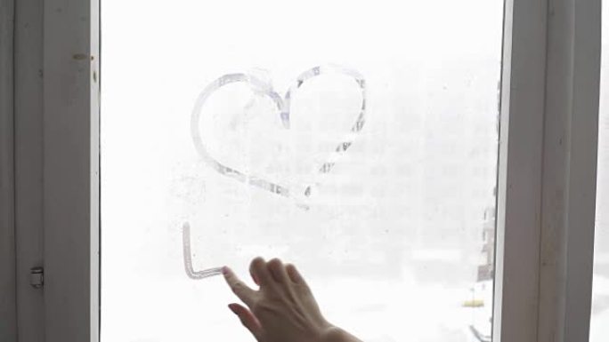 手在冷雾的窗户背景上绘制爱心，特写图像。