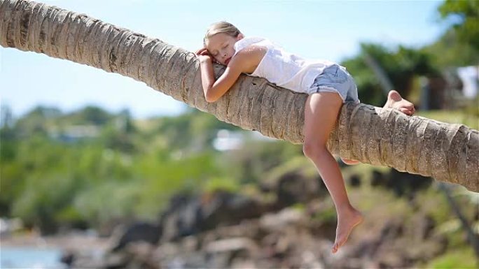 暑假期间，热带海滩上的小女孩坐在棕榈树上
