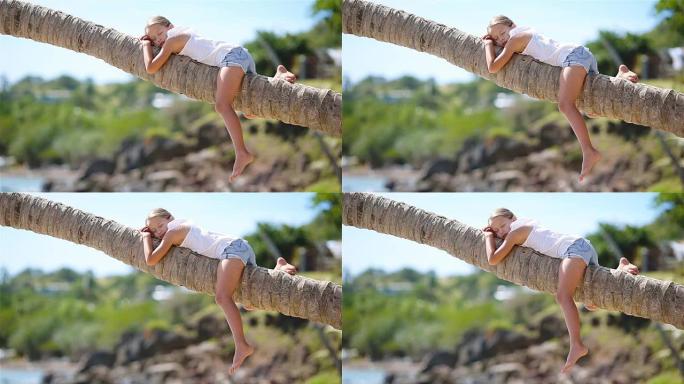 暑假期间，热带海滩上的小女孩坐在棕榈树上
