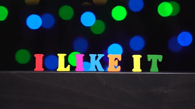 彩色单词 “我喜欢它” 来自抽象模糊灯光前的多色木制字母bokeh背景