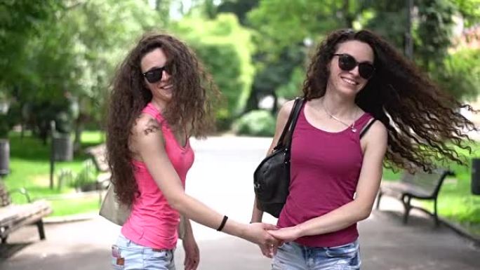 卷发双胞胎姐妹牵着手在城市公园散步