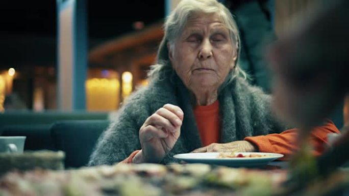 美丽的老妇人坐在餐厅里吃披萨。女性在咖啡馆将披萨切成碎片