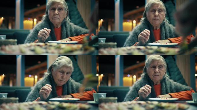 美丽的老妇人坐在餐厅里吃披萨。女性在咖啡馆将披萨切成碎片