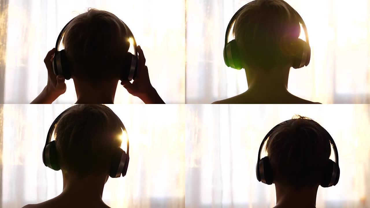 一个年轻人站在窗户附近，戴上耳机听音乐。日落背景模糊，青少年在耳机中享受音乐。