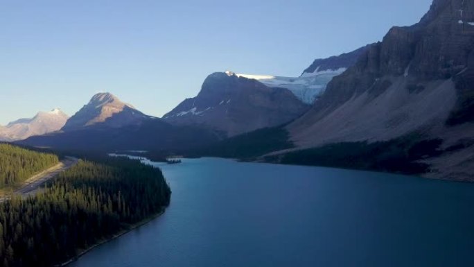 加拿大落基山脉日落时，在湖上的空中拍摄，毗邻山脉和森林的道路