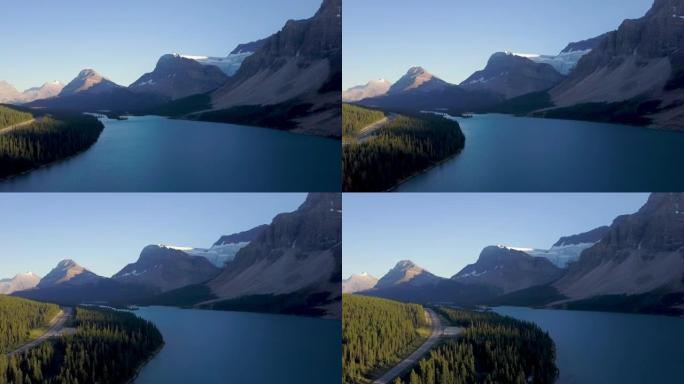 加拿大落基山脉日落时，在湖上的空中拍摄，毗邻山脉和森林的道路