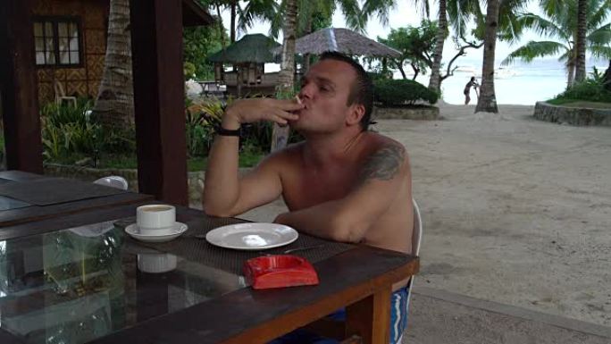 一个男人坐在街上的桌子旁，喝杯咖啡，抽烟