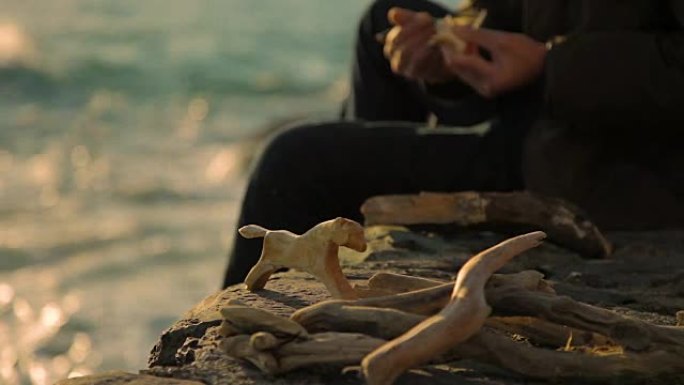 老人在日落时在海边雕刻木雕