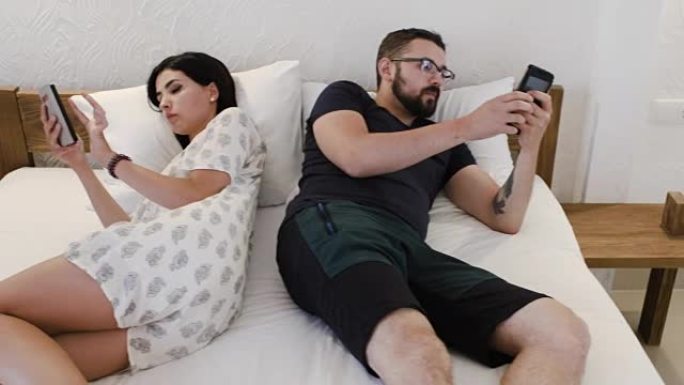 一对夫妇躺在床上，分别在手机上阅读东西的景象