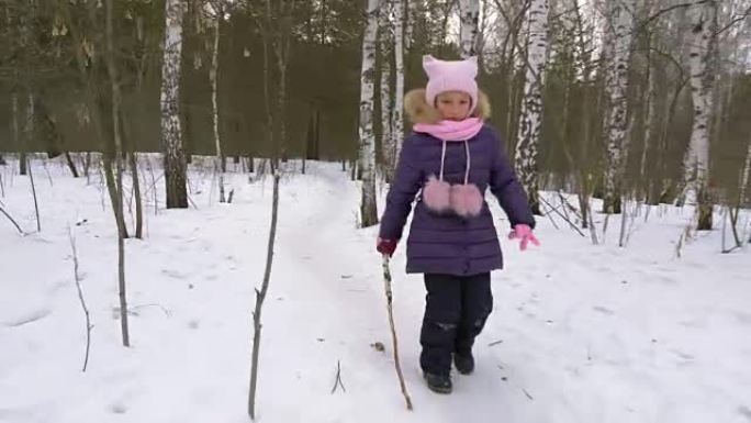 小女孩在冬季森林里沿着小路奔跑。女孩克服障碍。手拿棍子的女孩站起来走路。