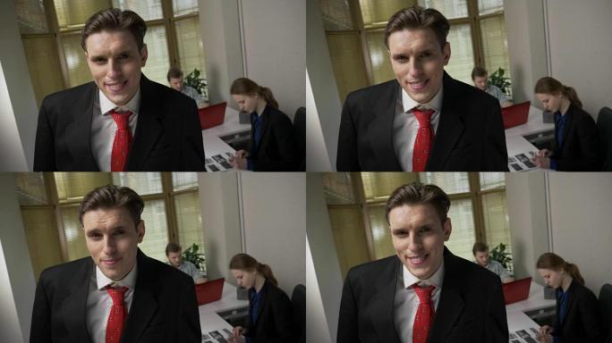 穿着西装的年轻人微笑着，摇摇头，看着镜头，背景中的男人和女孩正在办公室工作。是的，手势。60 fps