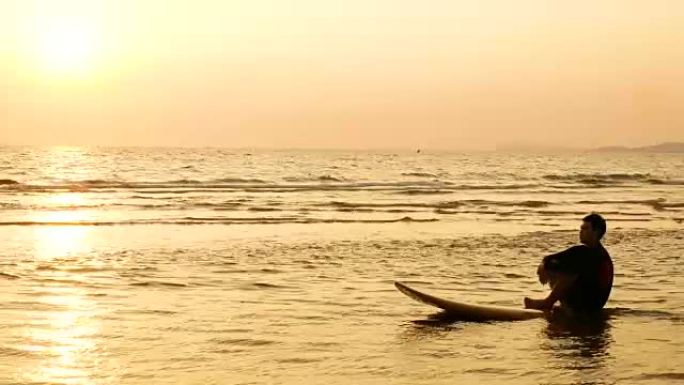 4K。冲浪者的剪影在热带海滩日落时坐在海上冲浪板上放松。夏季运动和娱乐概念