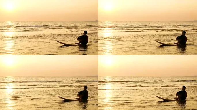 4K。冲浪者的剪影在热带海滩日落时坐在海上冲浪板上放松。夏季运动和娱乐概念