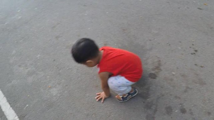 小男孩坐着，在沥青路面上玩耍