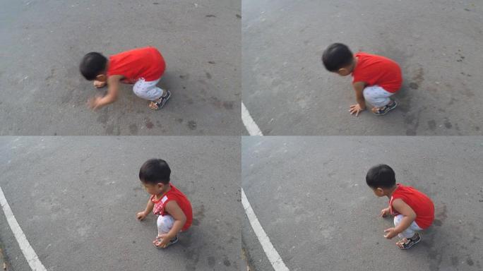 小男孩坐着，在沥青路面上玩耍