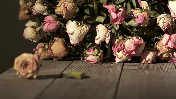 木桌上一束枯萎的玫瑰花。干粉色奶油黄色玫瑰