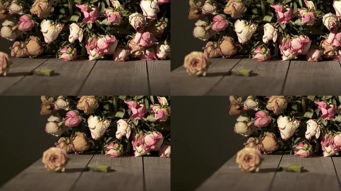 木桌上一束枯萎的玫瑰花。干粉色奶油黄色玫瑰