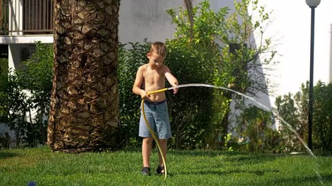 男孩在给草坪浇水时试图应付喷水