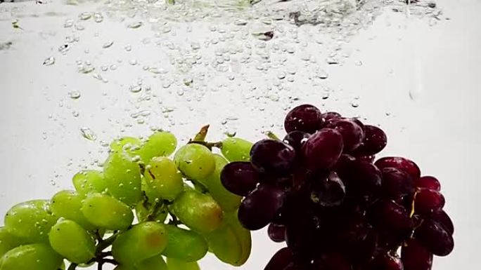 红色和绿色的葡萄在慢动作中带着气泡落入水中。白色背景上的水果。
