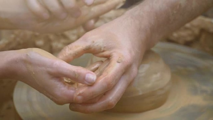两只交织在一起的手在陶工的轮子上形成一锅粘土。