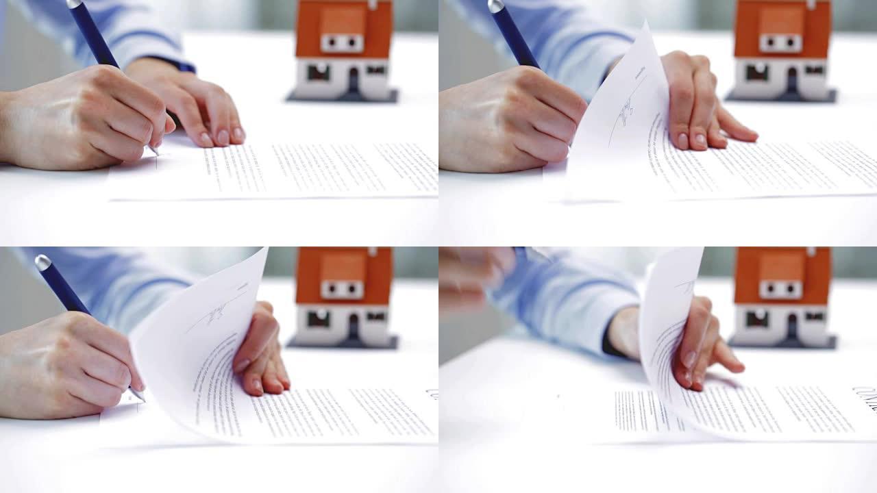 有房子模型和笔在办公室签署合同文件的女商人