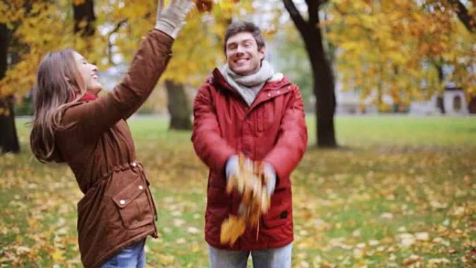 幸福的年轻夫妇在公园里扔秋叶